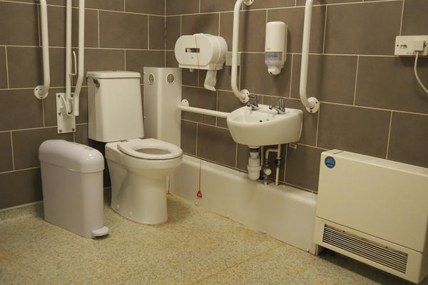 A view of the South accessible toilet. When seated on the toilet there is an emergency pull cable on the left. The sink is on the left.