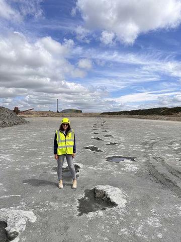 Dewars farm sauropod dinosaur trackway with Professor Kirsty Edgar of the University of Birmingham Professor Kirsty Edgar in hi-viz jacket standing beside a trail of sauropod footprints leading into the distance